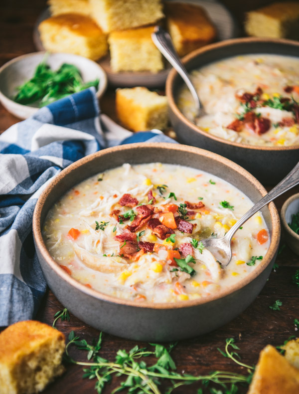 Side shot of a bowl of corn soup with bacon chicken on a table
