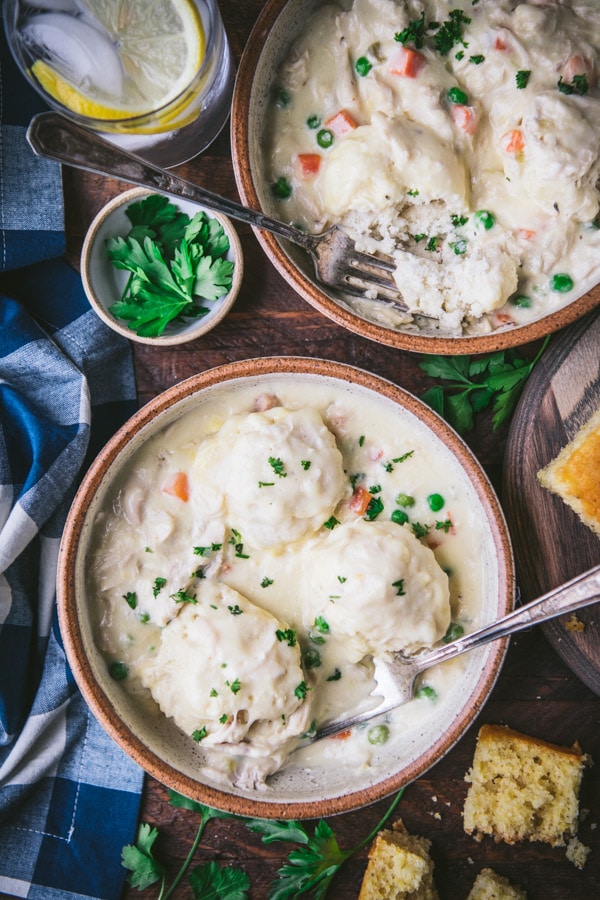 An overhead shot of two bowls filled with creamy chicken and dumplings. The light and fluffy dumplings are made with bisquick and cooked with peas and carrots in a soup gravy.