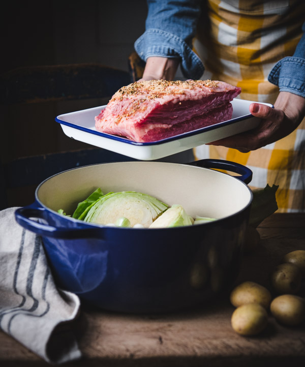 Process shot showing how to make corned beef and cabbage in a blue Dutch oven