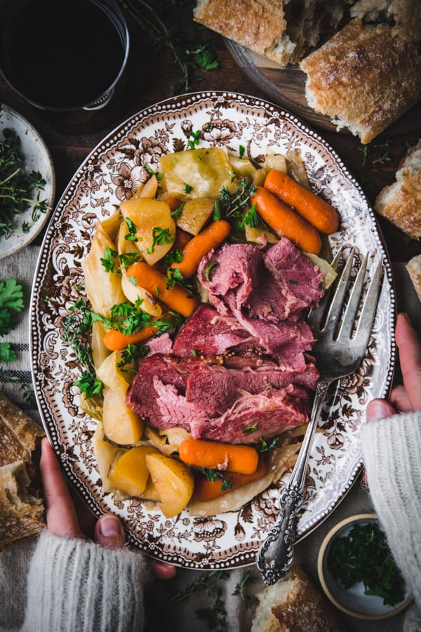 Overhead shot of hands holding a plate of the best corned beef and cabbage recipe.