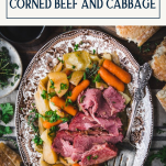 Overhead image of a platter of corned beef and cabbage on a dinner table with a side of bread and text title box at top.