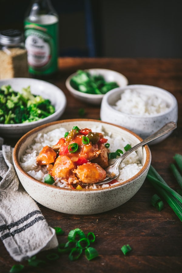 Side shot of a bowl of baked sweet and sour chicken served with rice and broccoli.