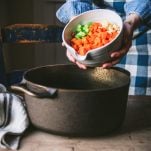 Adding diced vegetable to a cast iron pot.