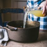 Pouring chicken broth into a Dutch oven.