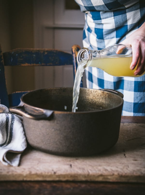 Pouring chicken broth into a Dutch oven.