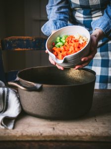 Adding diced vegetable to a cast iron pot.
