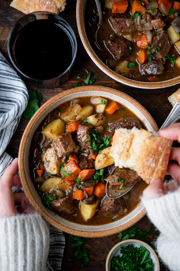 Hands eating a bowl of lamb stew with a piece of bread