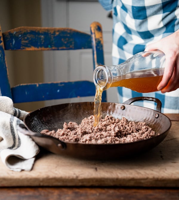 Pouring beef broth into a skillet.