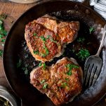 Close overhead image of two pan fried pork chops in a cast iron skillet