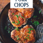 Close overhead image of two pan fried pork chops in a cast iron skillet with text title overlay
