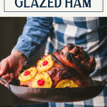 Hands holding a pineapple glazed ham in a roasting pan with text title box at top.