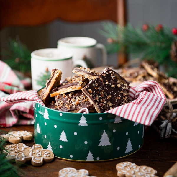 A square-cropped image of a Christmas cookie tin filled with squares of homemade saltine cracker toffee.