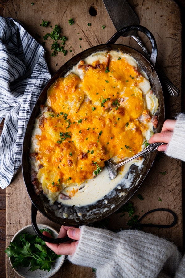 Hands serving scalloped potatoes from a cast iron dish