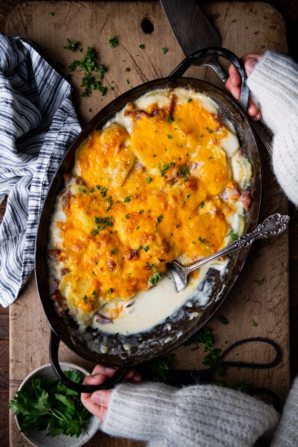 Hands holding a dish of cheesy scalloped potatoes and ham