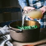 Pouring chicken broth into a dutch oven.