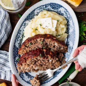 Overhead shot of hands eating a southern style meatloaf recipe with a bite on a fork