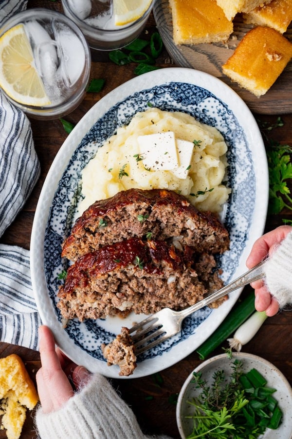 Overhead shot of hands eating a southern style meatloaf recipe with a bite on a fork