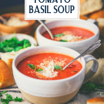 Side shot of two bowls of creamy tomato basil soup with text title overlay