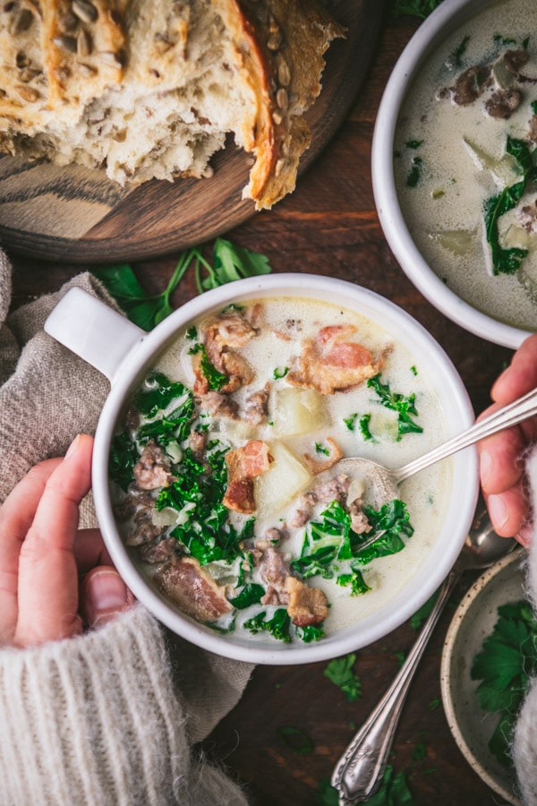 Hands using a spoon to eat a bite of Zuppa Toscana soup.