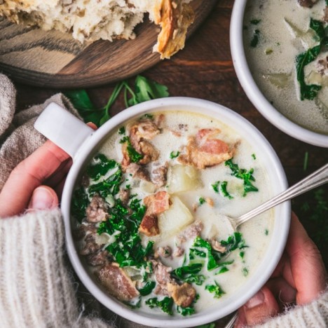 Overhead image of hands holding Zuppa Toscana in a white bowl.