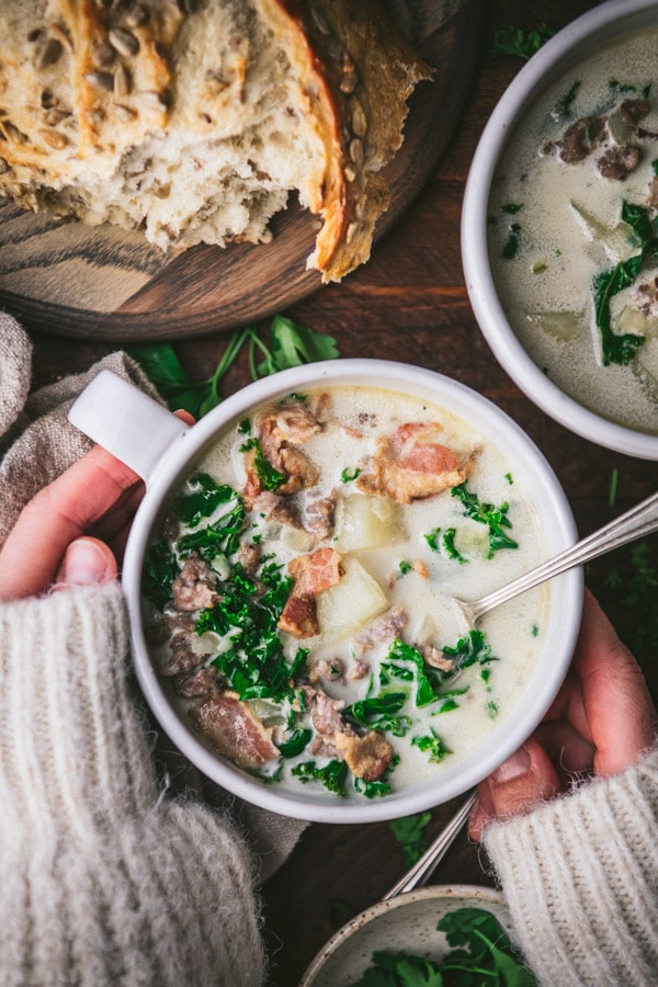 Overhead image of hands holding Zuppa Toscana in a white bowl.