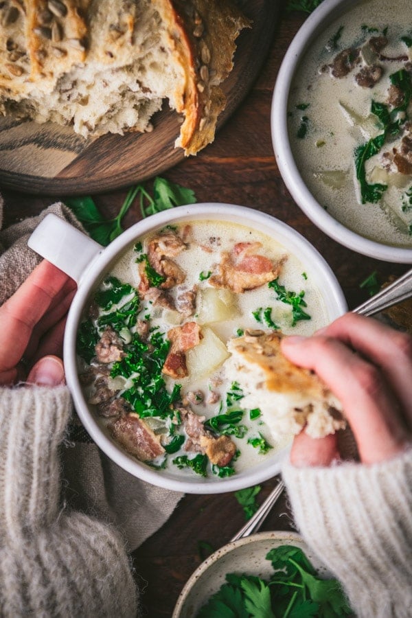 Overhead image of hands dipping bread in a bowl of Olive Garden copycat zuppa toscana.