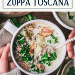Hands eating a bowl of zuppa toscana with text title box at top