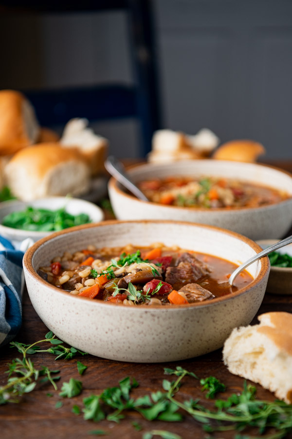 Side shot of two bowls of beef and barley soup on a table with bread.