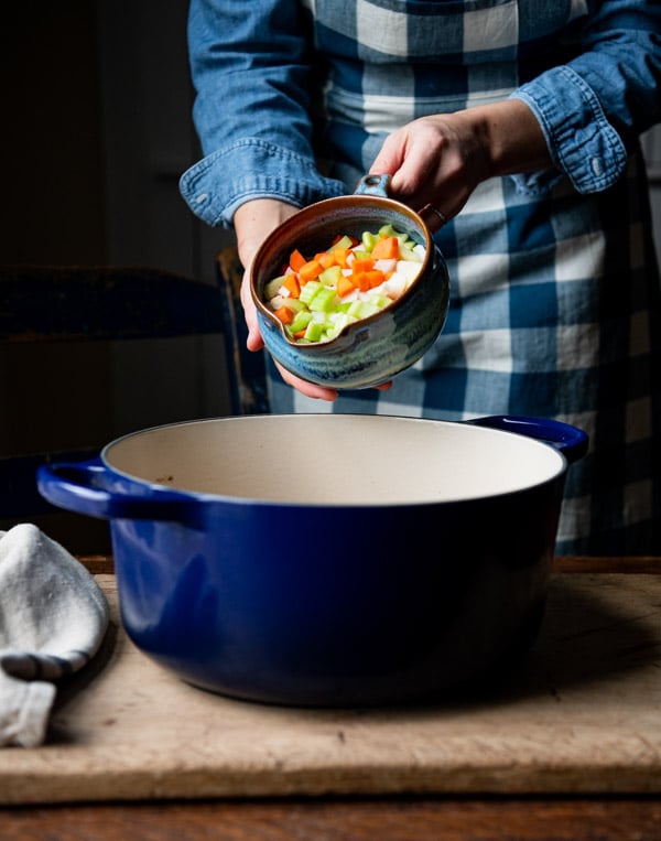 Adding vegetables to a Dutch oven.