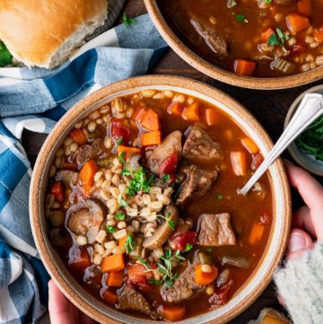Hands holding a bowl of the best beef barley soup recipe.