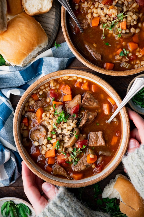 Hands holding a bowl of the best beef barley soup recipe.