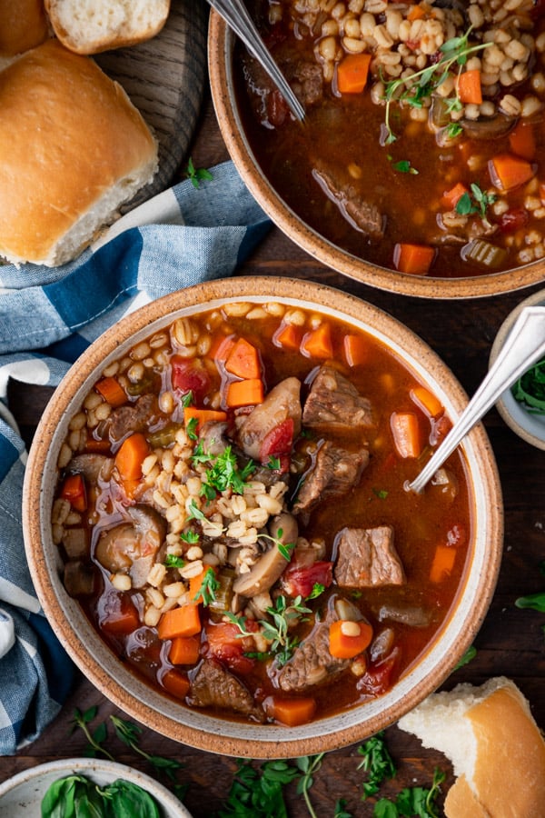 Overhead image of beef and barley soup in a bowl with a side of bread.