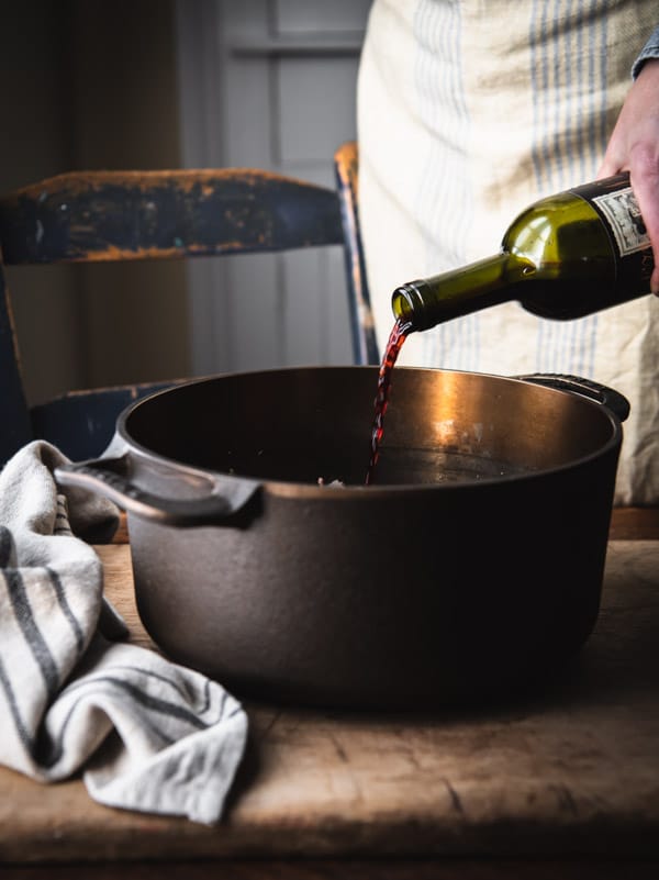 Pouring red wine into a Dutch oven.