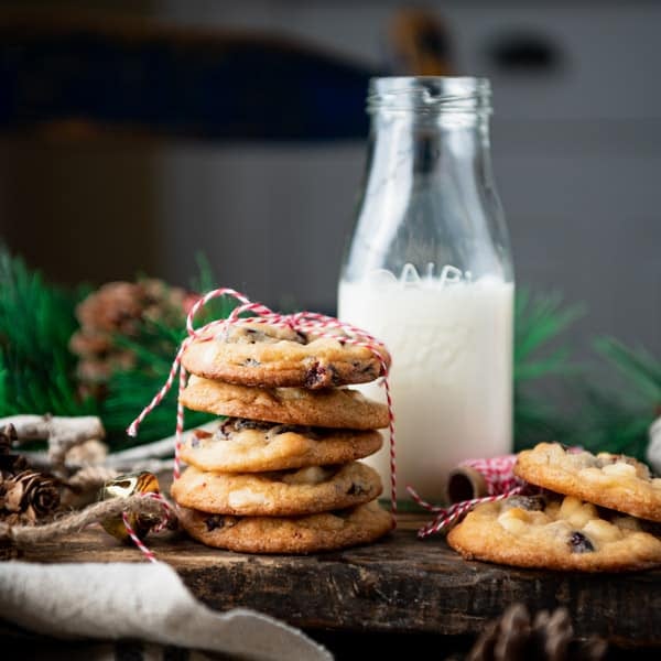Square side shot of cranberry and white chocolate chip cookies on a wooden table with a glass of milk