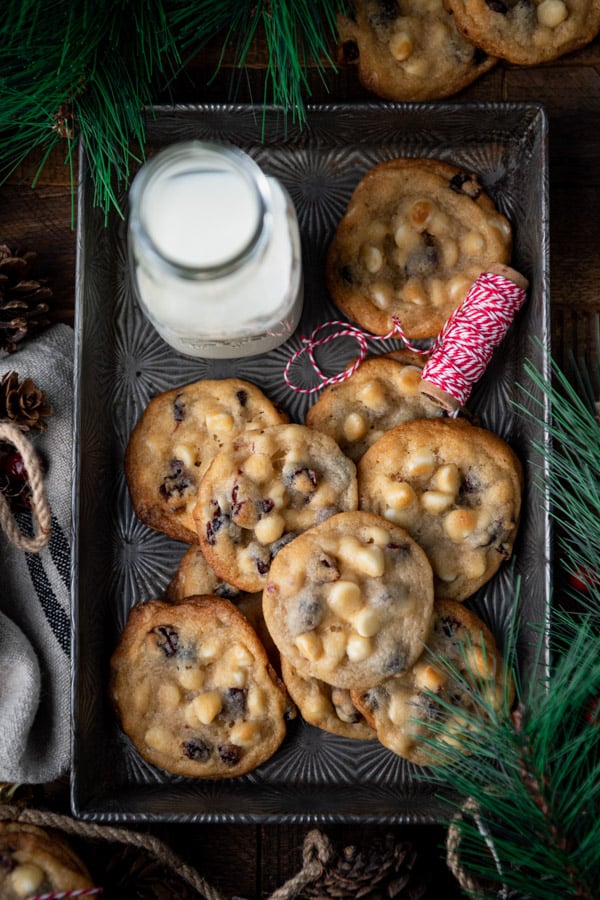 Overhead shot of white chocolate chip cookies in a metal pan with a glass of milk