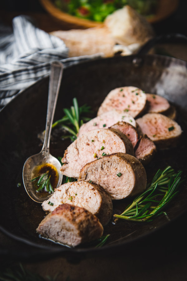Close up side shot of garlic and rosemary baked pork tenderloin sliced in a pan
