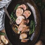 Overhead image of sliced baked pork tenderloin in a pan with fresh rosemary