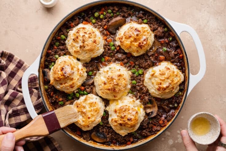 Brushing garlic butter on top of the biscuits on the ground beef pot pie.