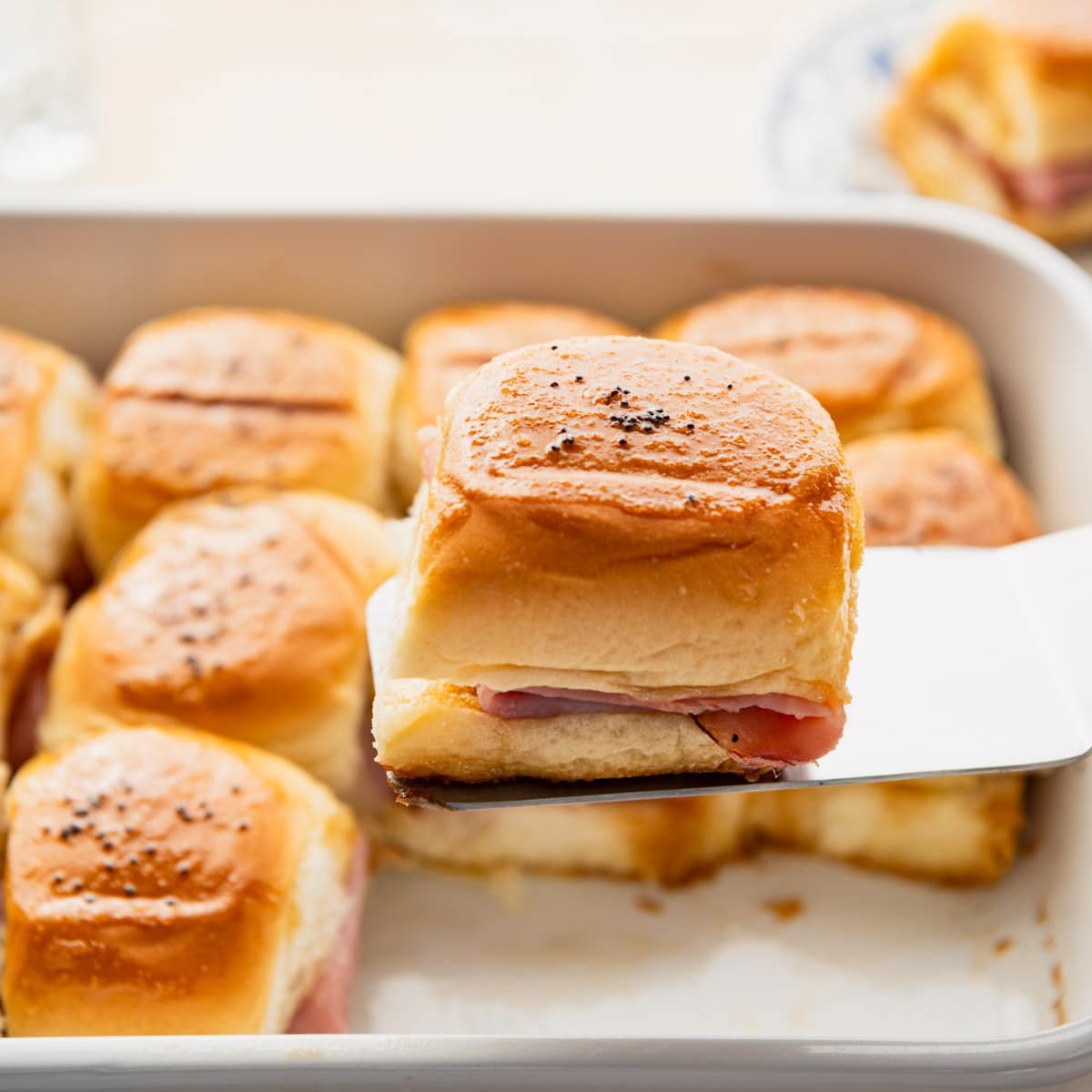 Spatula serving ham and cheese sliders.