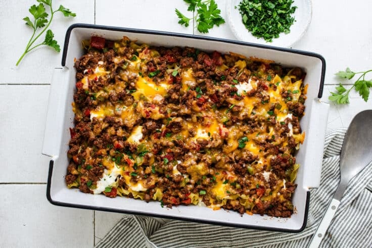 Horizontal overhead shot of a hamburger casserole with noodles and sour cream in a white baking dish.