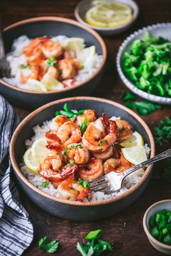 Side shot of two bowls of honey garlic shrimp on rice on a dinner table.