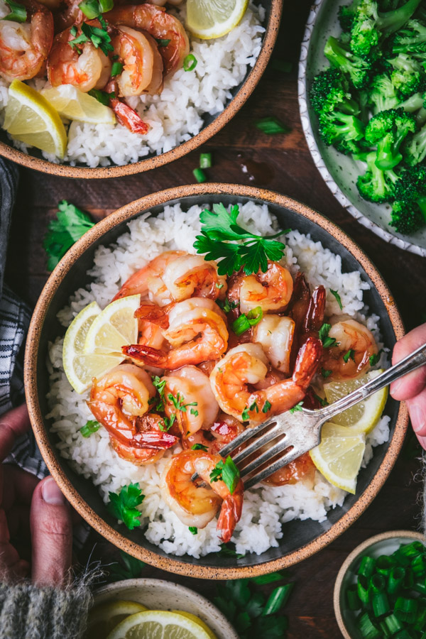 Overhead shot of honey garlic shrimp stir fry in a bowl with rice and lemon wedges