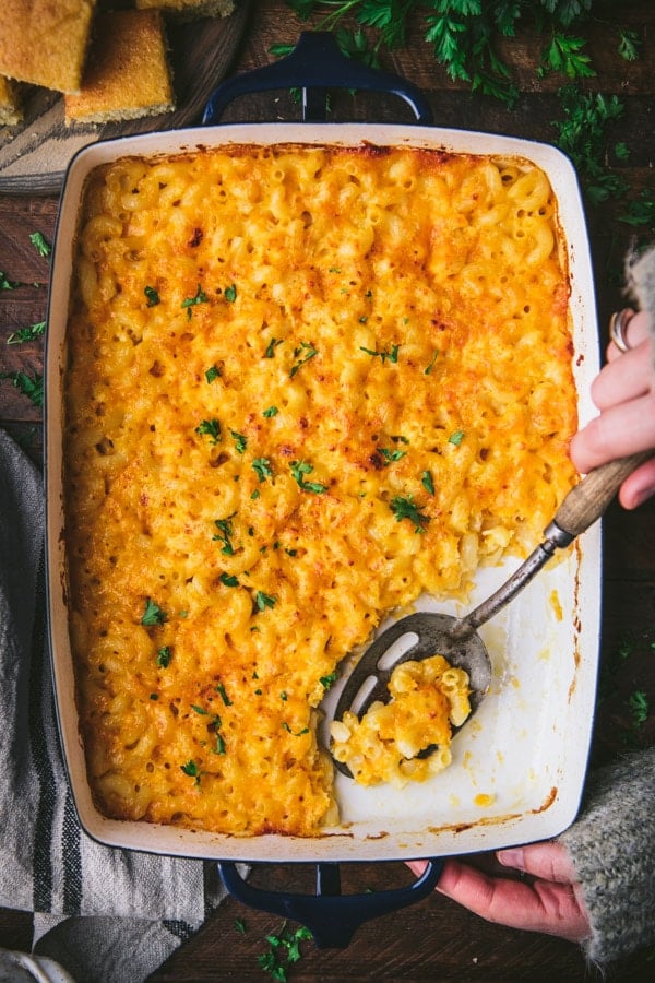 Hands serving a pan of easy macaroni cheese with parsley garnish.