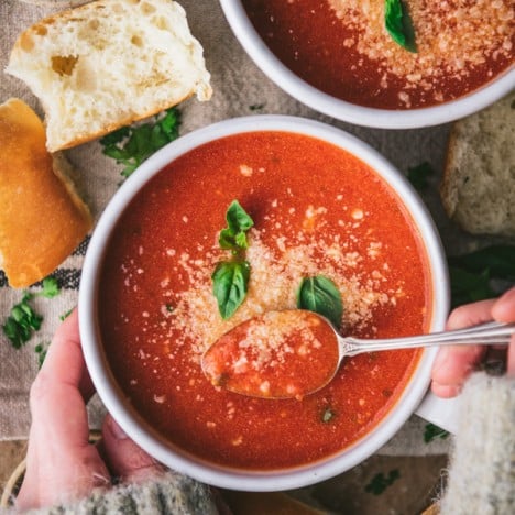Overhead image of hands eating a bowl of homemade tomato basil soup.