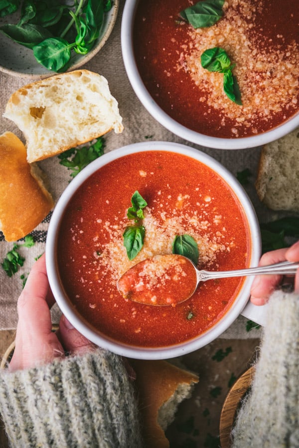 Overhead image of hands eating a bowl of homemade tomato basil soup.