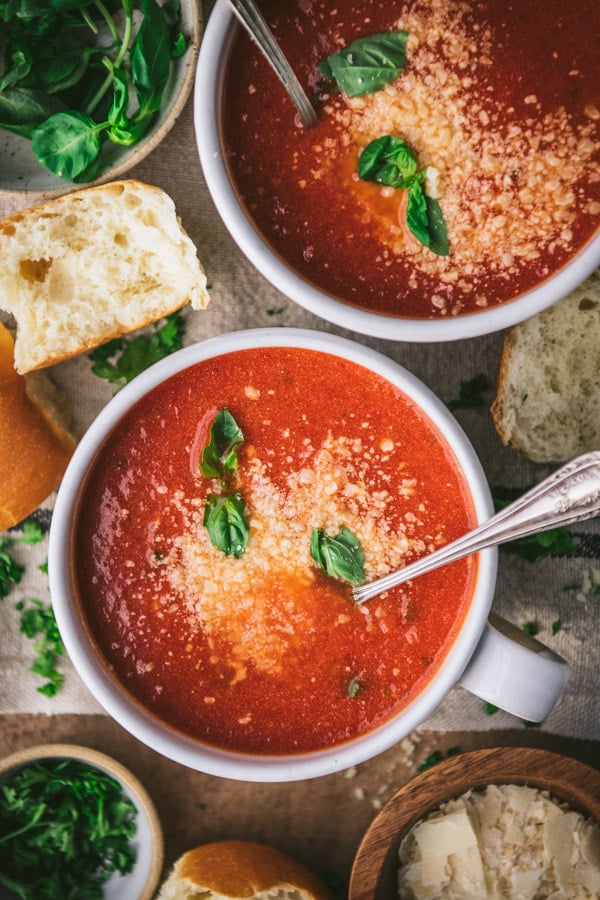 Close overhead shot of a spoon in a bowl of tomato soup with parmesan cheese and fresh basil on top.