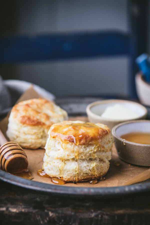 Side shot of buttermilk biscuits on a tray with honey drizzled over top