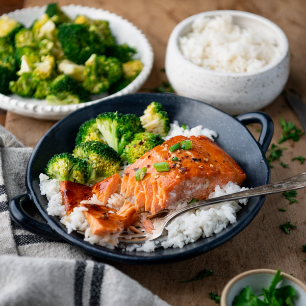 Flakey, tender baked salmon served in a bowl over a bed of white rice and steamed broccoli.