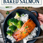 Overhead shot of hands holding a bowl of baked salmon with text title box at top