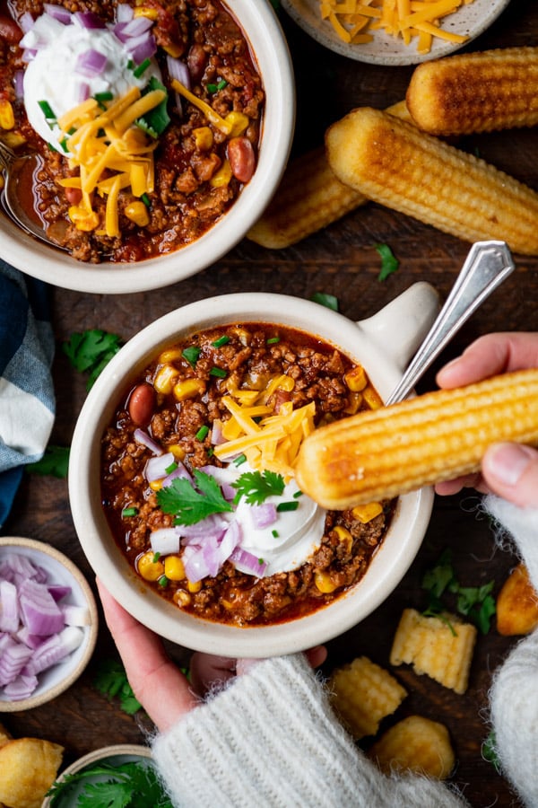 Hands dipping cornbread in a bowl of beef chili.